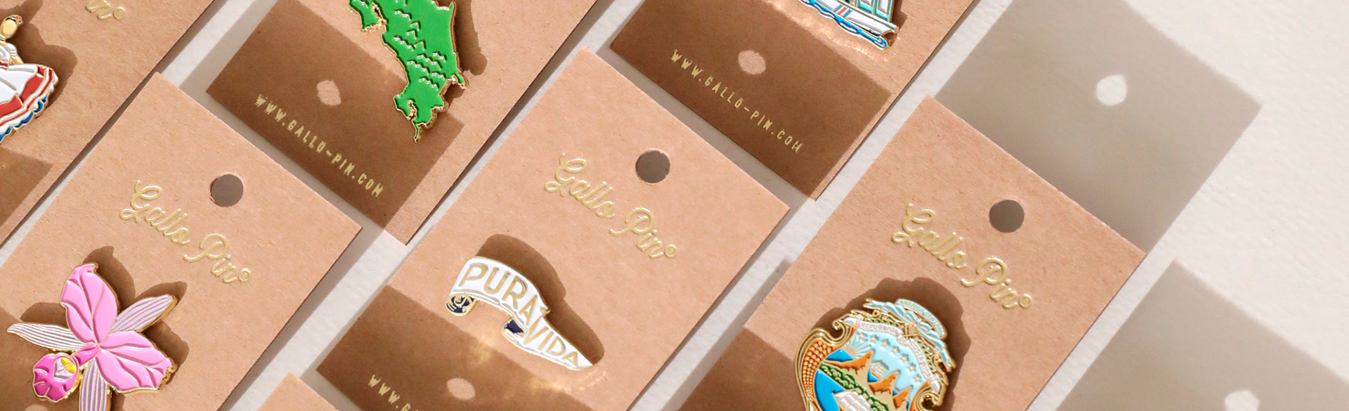 Pines esmaltados de Gallo Pin sobre tarjetas kraft con logo dorado